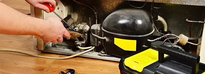 Refrigerator repair technician fixing the compressor and wiring in Tea, SD