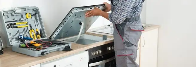 Cooktop repair technician lifting a built-in stovetop for service in Sioux Falls, SD