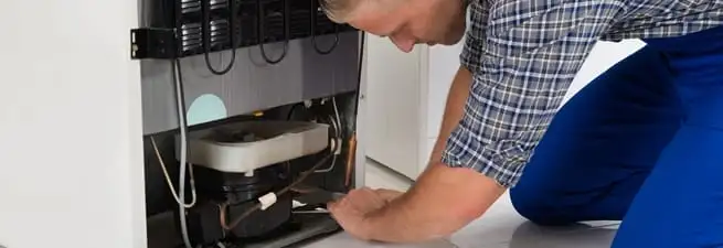 Refrigerator repair technician servicing the compressor and condenser area in Sioux Falls, SD