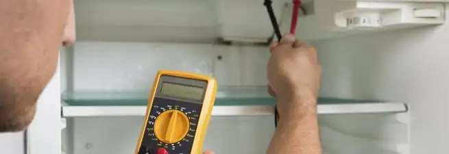 Refrigerator repair technician testing electrical components with a multimeter in Sioux Falls, SD
