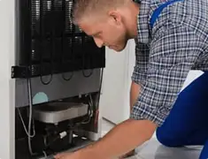 Refrigerator repair technician servicing the compressor and condenser area in Sioux Falls, SD